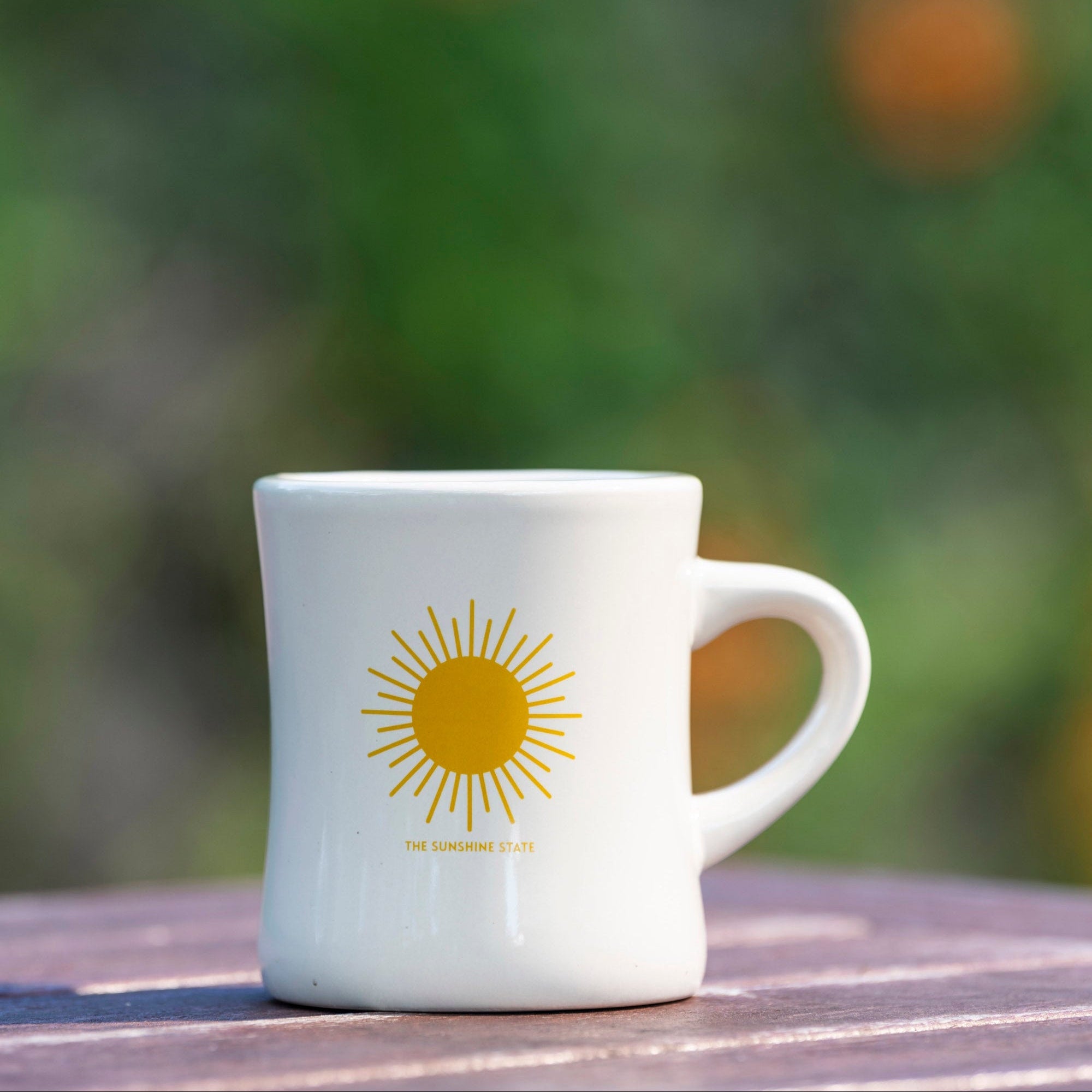 White mug with a yellow sun design on a wooden surface with a blurred green background