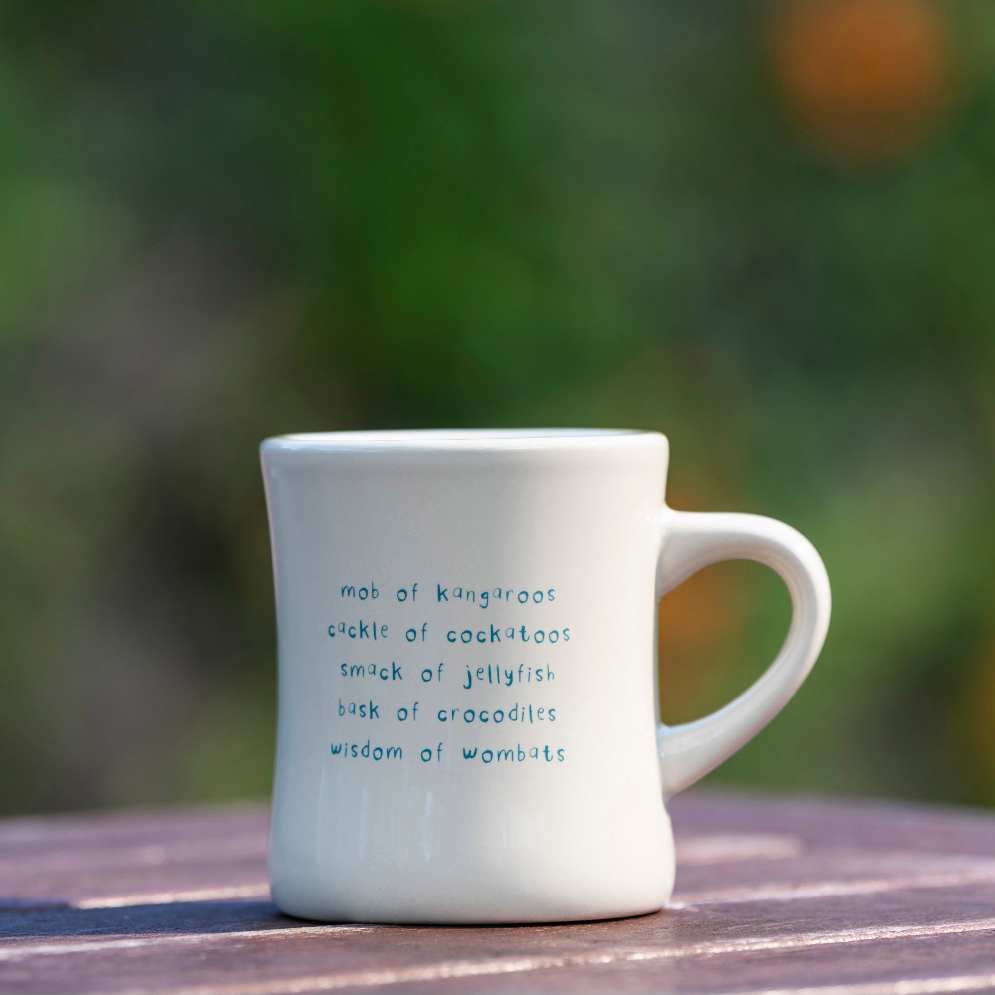 White mug with text on a wooden surface with a blurred natural background
